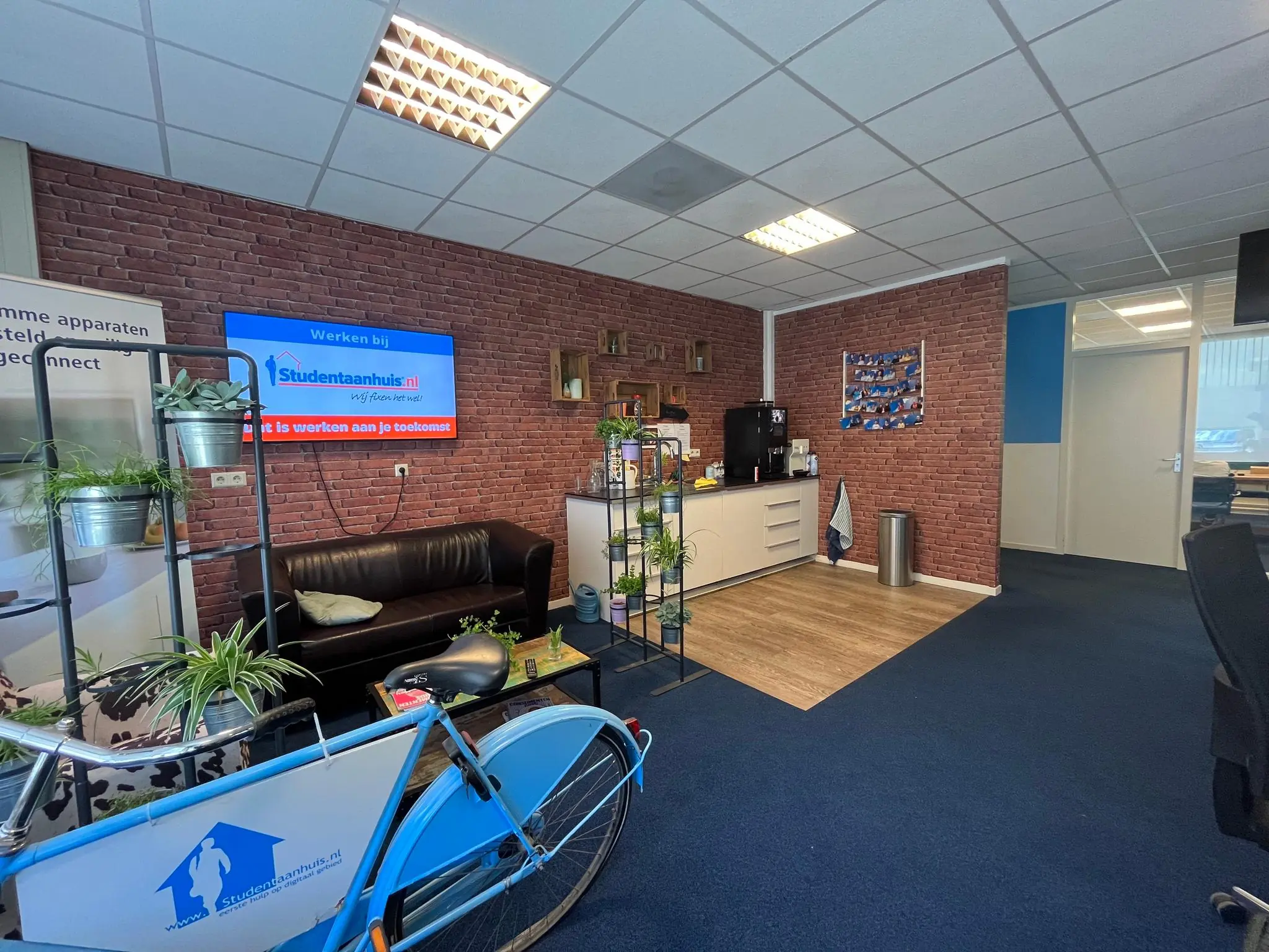 Kantoorruimte van Studentaanhuis.nl met een bank, koffiestation, bedrijfsfiets en opvallende bakstenen muur.